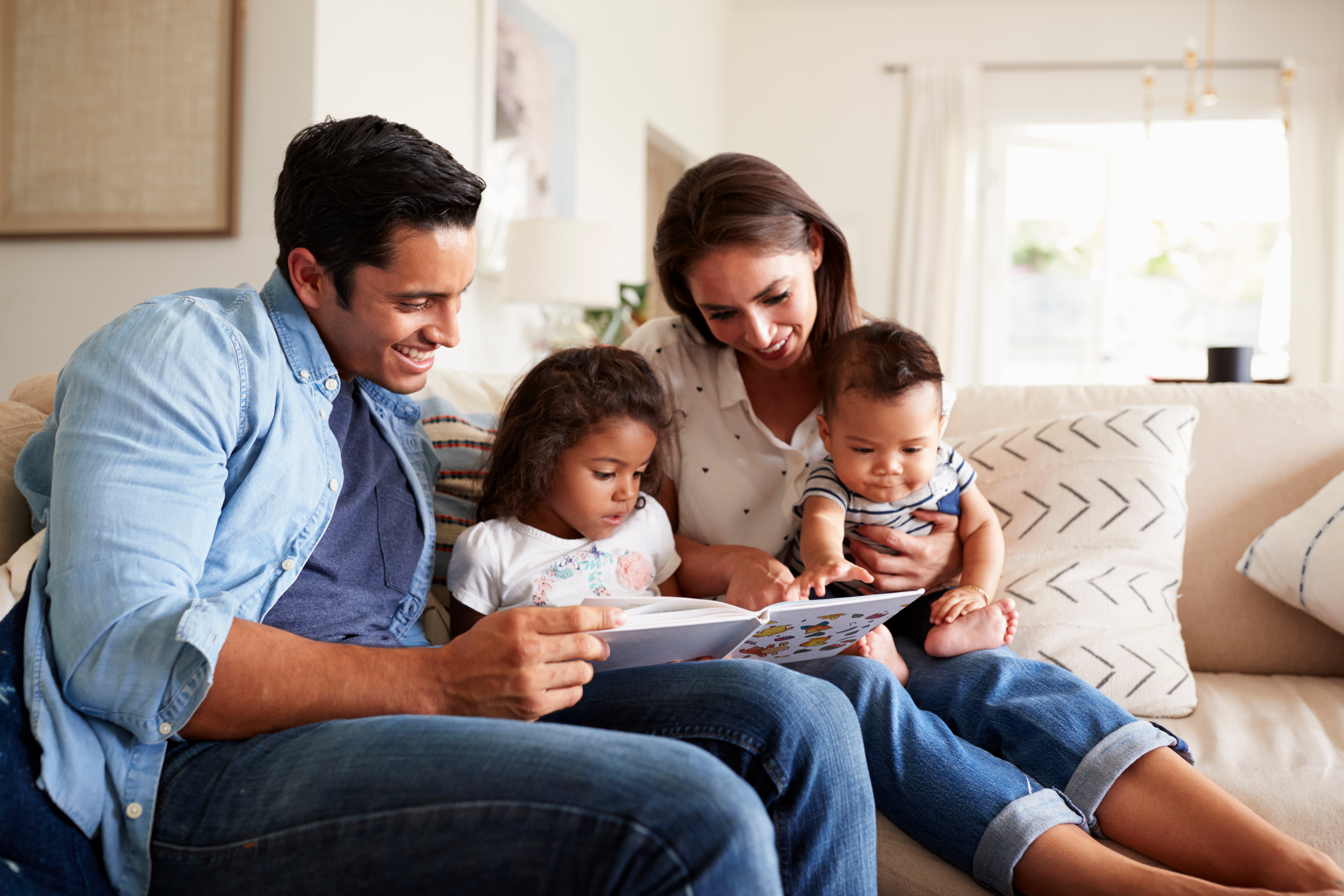 Family of 4 in living room, reading a children's book